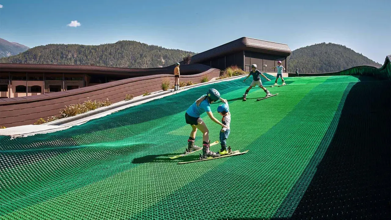 Bambini imparano a sciare su una pista verde al Falkensteiner Family Resort Lido, con montagne sullo sfondo.
