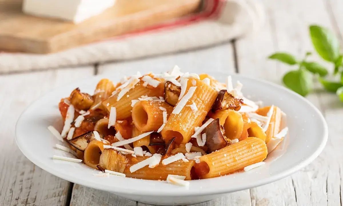Un piatto invitante di pasta alla norma con melanzane fritte, pomodoro e ricotta salata grattugiata, pronto per essere gustato.