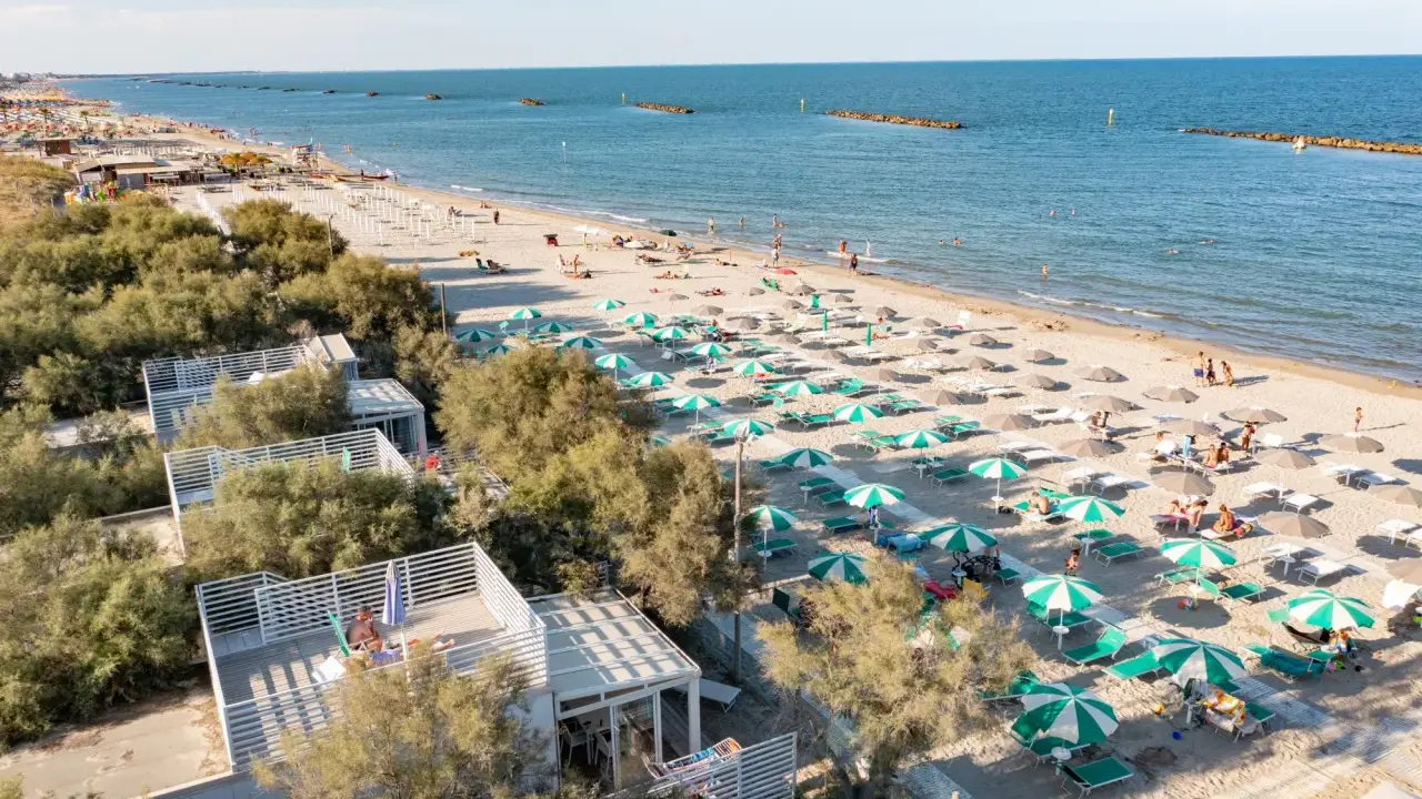 Lidi ferraresi: una distesa di ombrelloni verdi e bianchi sulla sabbia dorata, con il mare azzurro e alcune persone che si godono il sole.