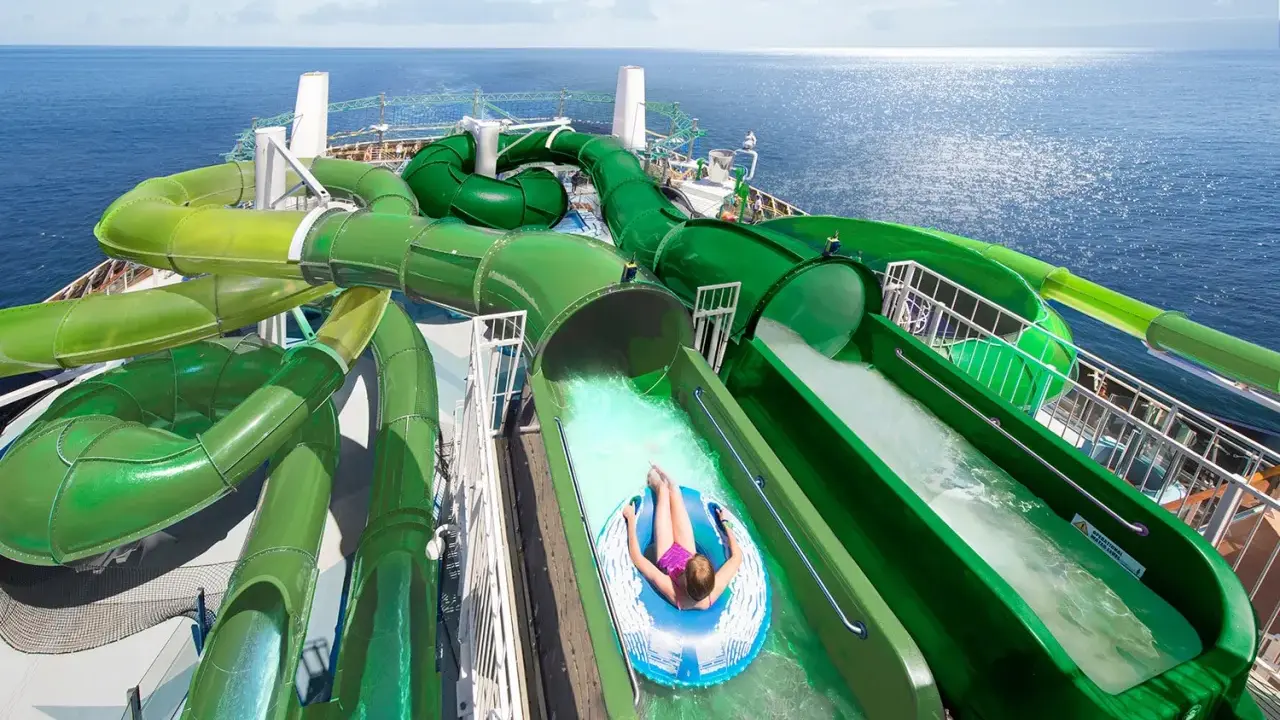 Divertente crociera per bambini con scivoli acquatici verdi che si snodano sul ponte di una nave da crociera, con il mare blu sullo sfondo.