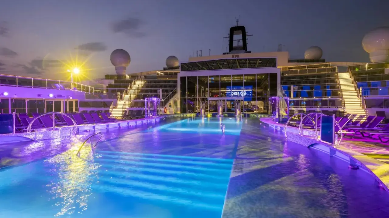 Piscine illuminate con luci viola e blu sulla MSC World Europa, con sdraio e scale illuminate.