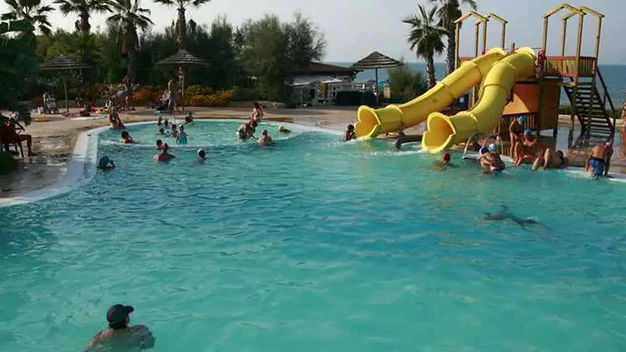 Piscina con scivoli gialli e persone che nuotano, ideale per campeggi puglia sul mare per bambini.