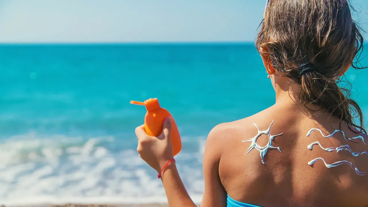 Bambina sulla spiaggia applica crema solare, disegnando un sole e onde sulla schiena. Un modo per non abbronzarsi e proteggersi.