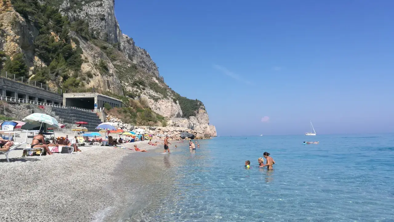 Varigotti spiaggia più bella: gente rilassata sotto gli ombrelloni, mare cristallino e scogliere imponenti.