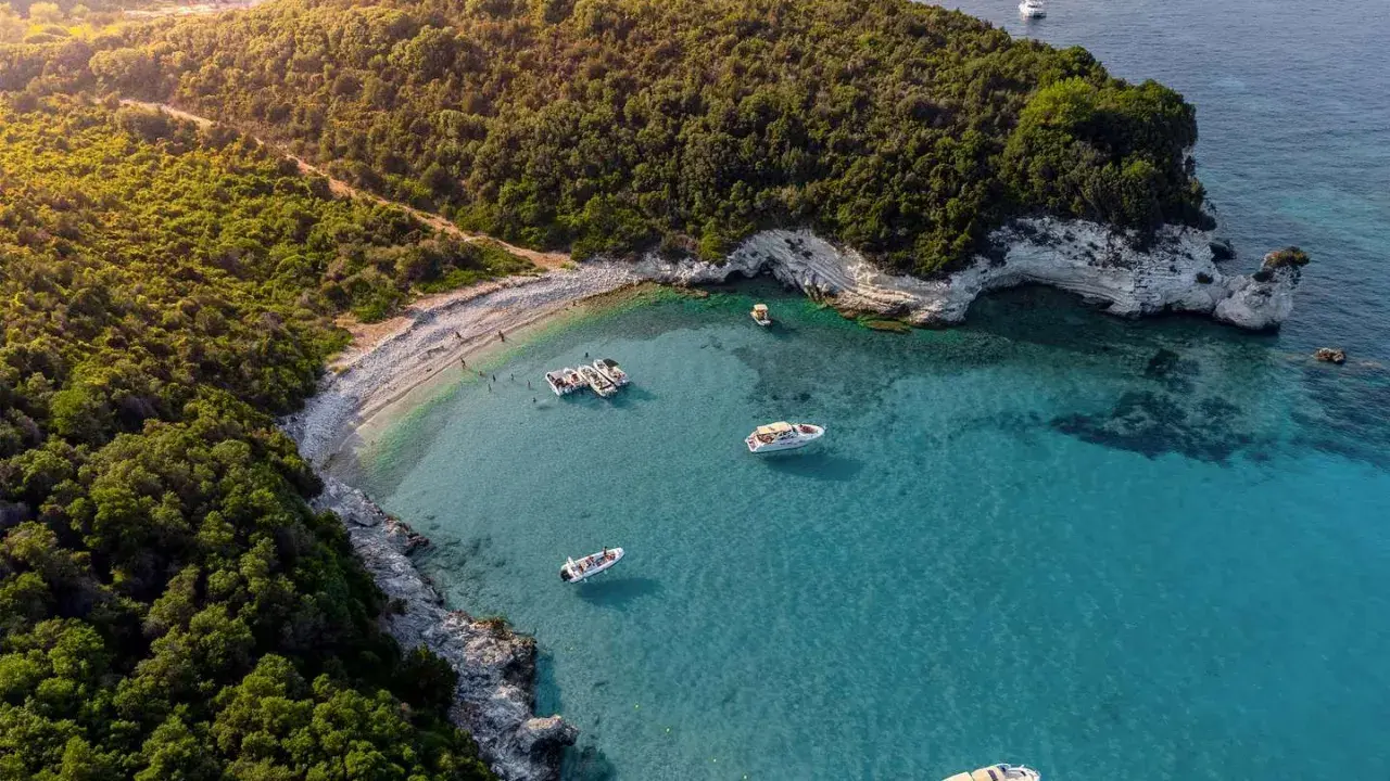 Baia con acque cristalline e vegetazione lussureggiante, ideale per famiglie. Diverse barche ormeggiate, perfette per esplorare le isole greche.