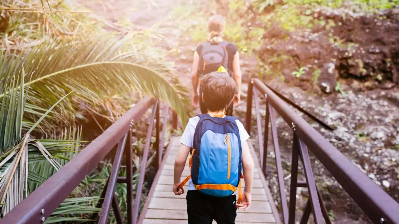 Bambini con zaini attraversano un ponte di legno in un sentiero lussureggiante, un'avventura perfetta per il tuo viaggio a Tenerife con bambini.
