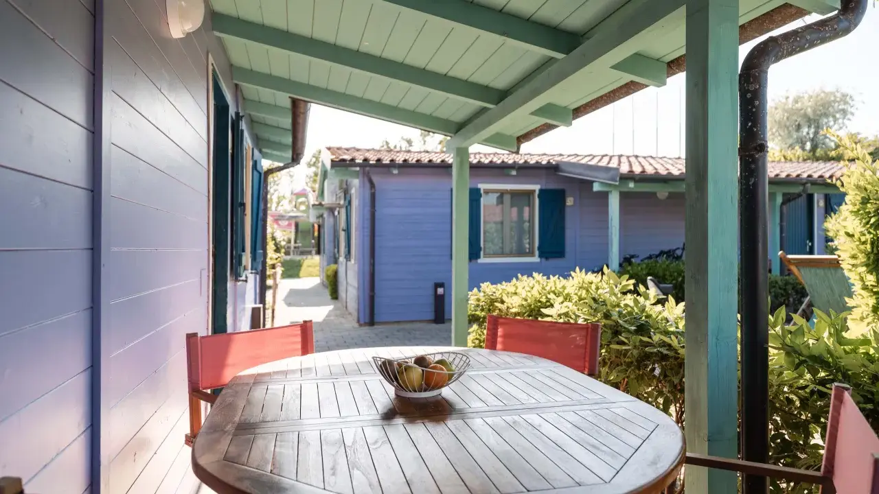 Tavolo con frutta su un portico colorato, con casette in stile villaggi Conero sul mare per bambini sullo sfondo.