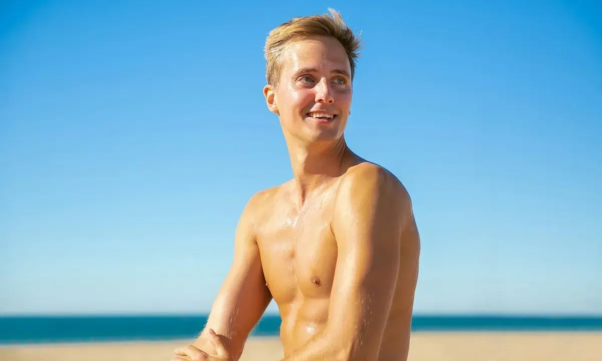 Giovane uomo sorridente sulla spiaggia, con la pelle dorata come se con l'autoabbronzante potesse prendere il sole senza rischi.