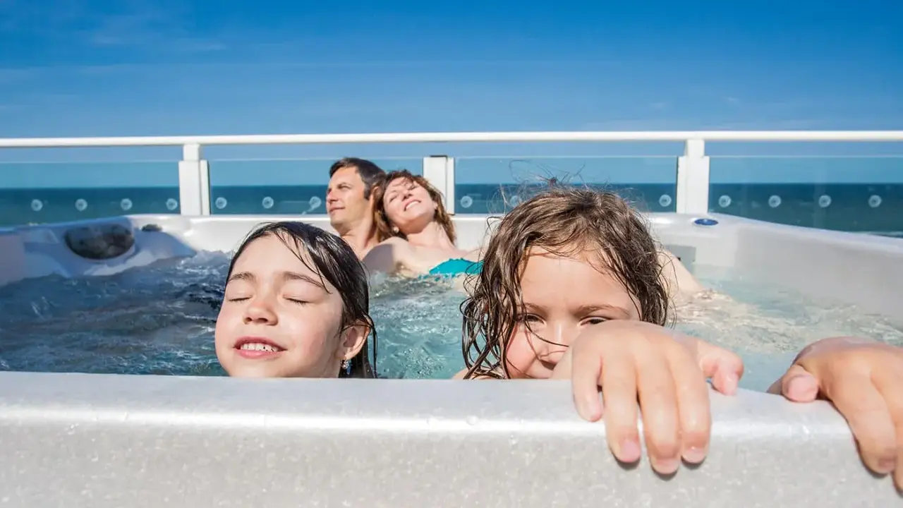 Famiglia felice in vasca idromassaggio, godendosi il Ferragosto con bambini. Il sole splende, il mare sullo sfondo.