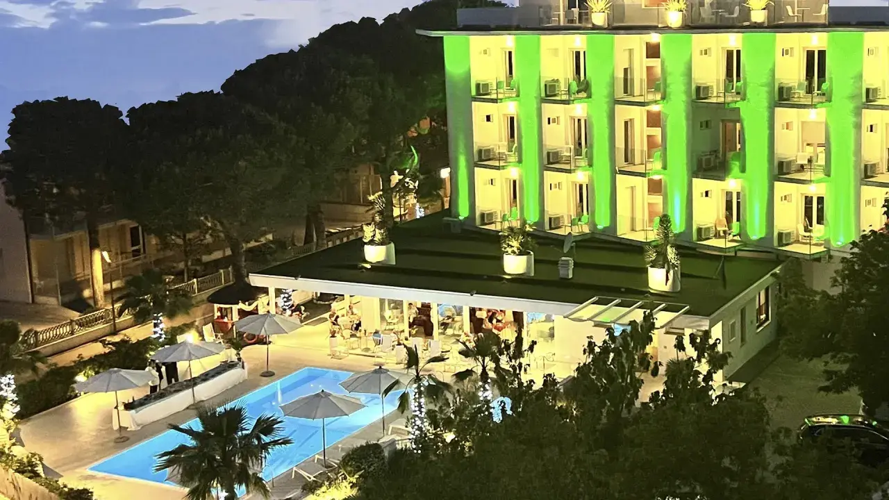 Hotel Biondi Cesenatico: piscina illuminata e facciata verde brillante. Le recensioni lodano l'atmosfera serale.