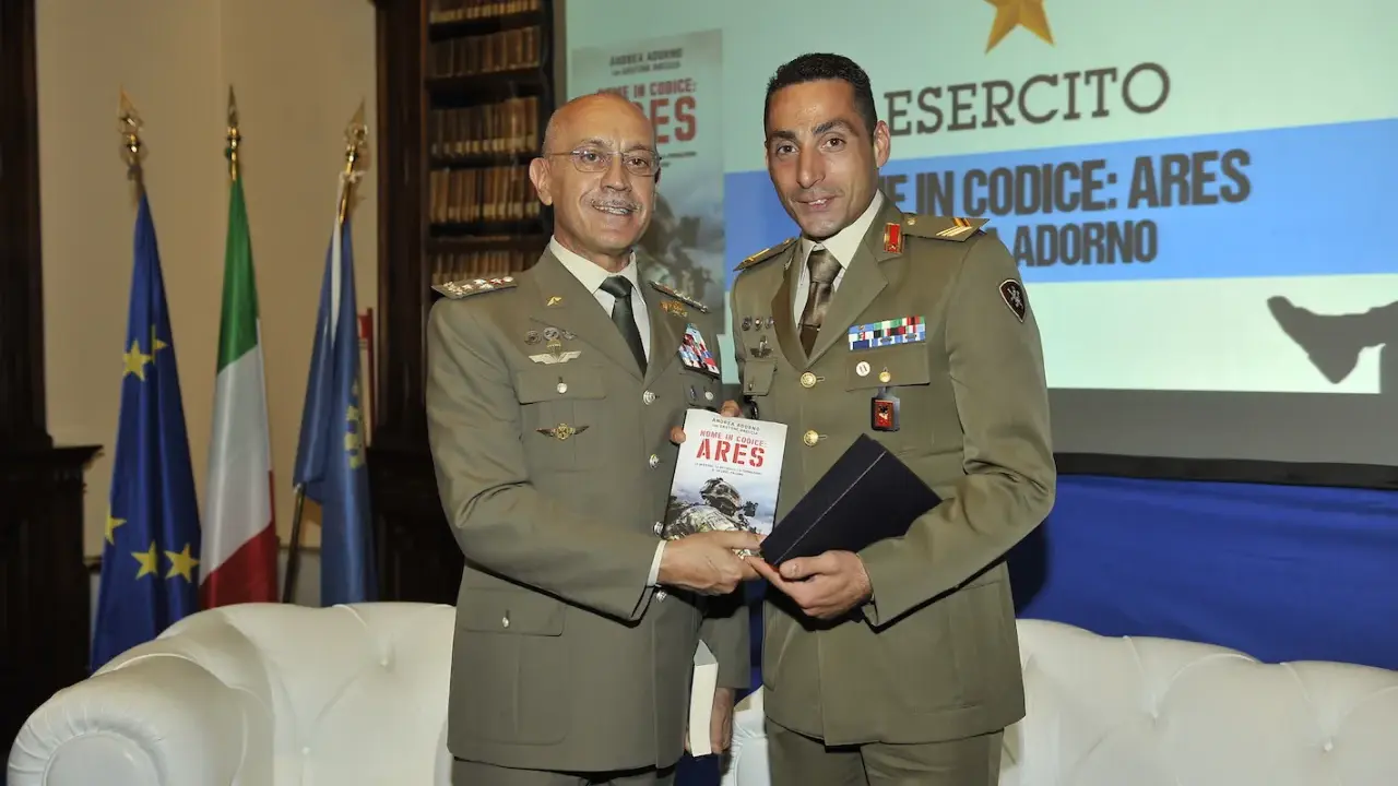 Due ufficiali in uniforme presentano un libro. Uno dei due, con un sorriso, tiene in mano il volume intitolato "Nome in codice: Ares", un'opera che narra storie di coraggio, forse ispirate a un vero pesce monaco.