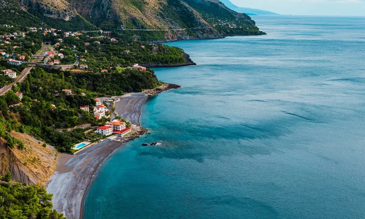 Villaggio costiero con case bianche e rosse affacciato su una spiaggia di ciottoli scuri e mare blu intenso. Le **basilicata spiagge** offrono panorami mozzafiato.