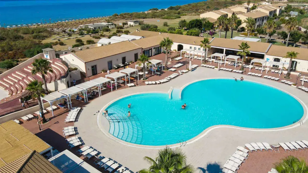Vacanze al Sikania Eco Resort: piscina azzurra, lettini, palme e il mare all'orizzonte.
