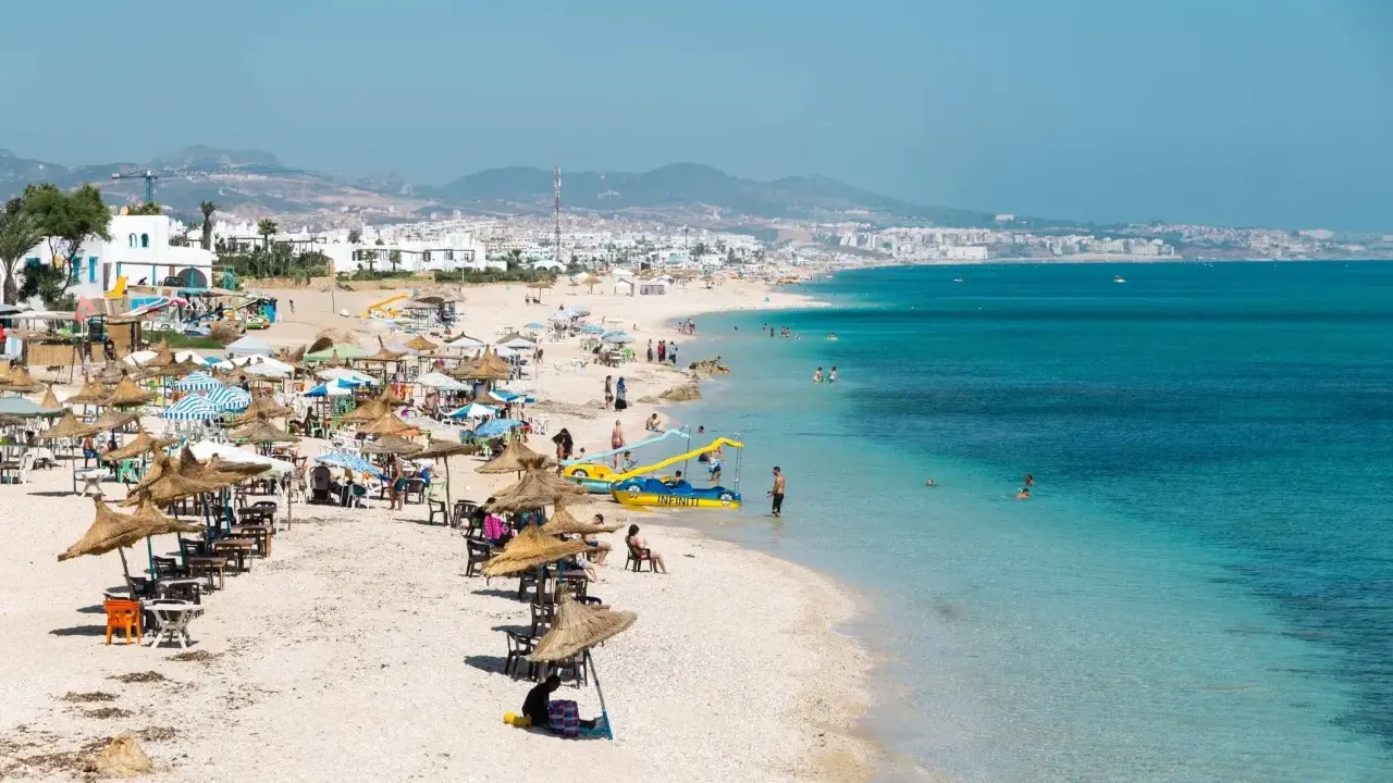Spiaggia affollata in Marocco con bambini che giocano in acqua e famiglie che si rilassano sotto gli ombrelloni.