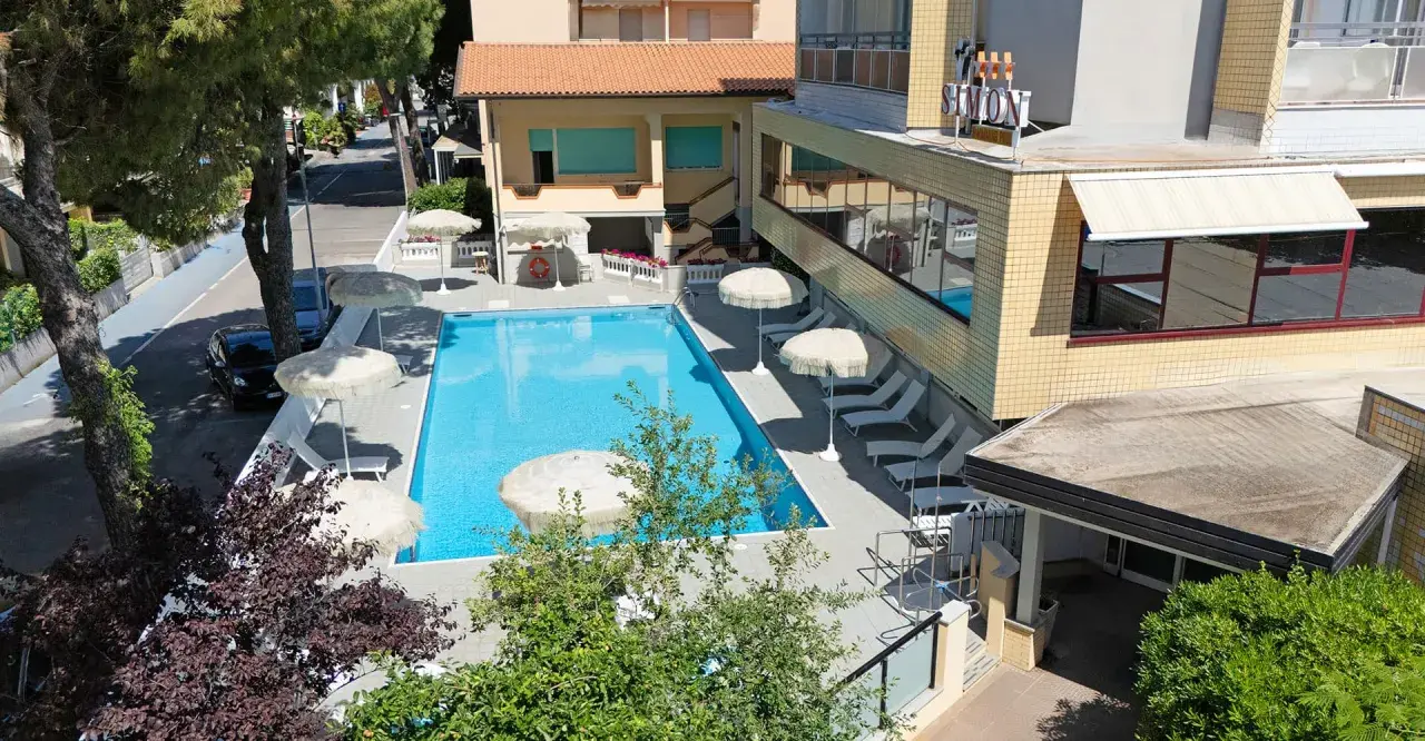 Piscina invitante e lettini prendisole al **hotel Simon Gatteo Mare**. Ombrelloni bianchi e vegetazione rigogliosa creano un'oasi di relax.