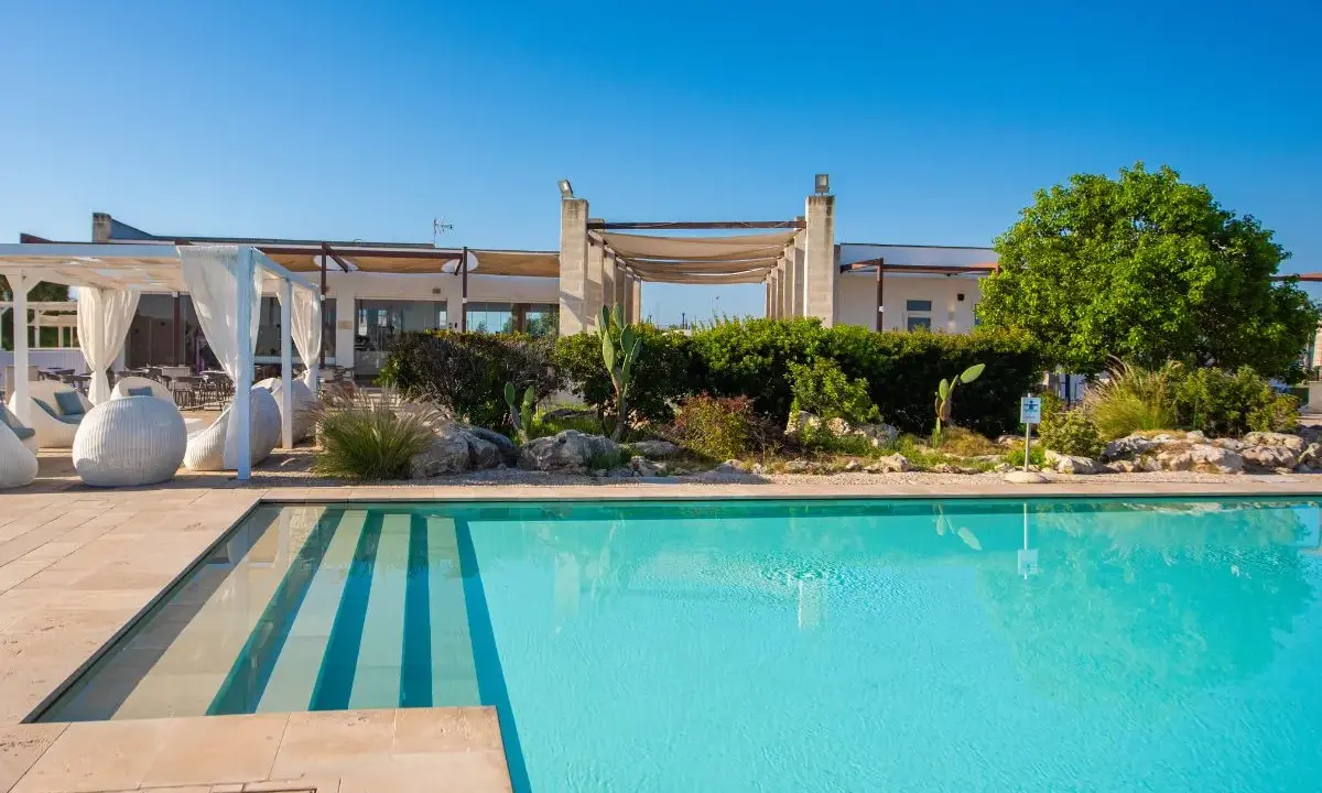 Piscina cristallina e lettini bianchi al le cesine resort, sotto un cielo azzurro. Relax e natura.