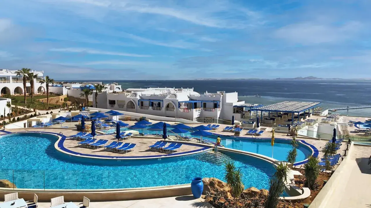 Vista panoramica del Futura Club Albatros Palace Sharm: piscine azzurre, lettini, ombrelloni blu e il mare scintillante all'orizzonte.