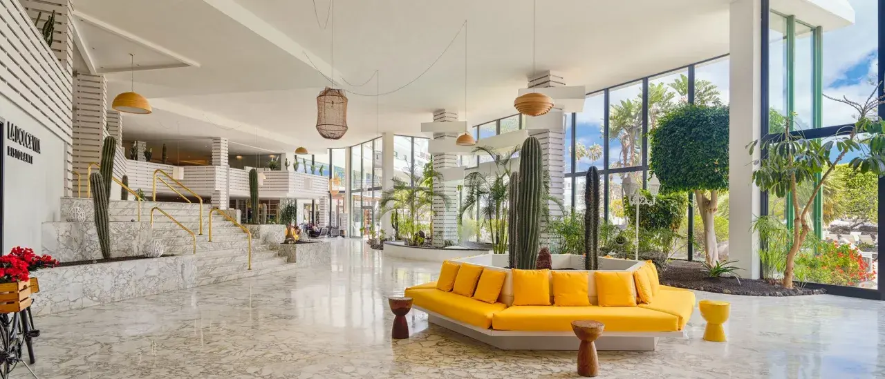 Lobby moderna con cactus e piante tropicali, divano giallo vivace e marmo lucido. Un'oasi di stile al H10 Lanzarote Princess.