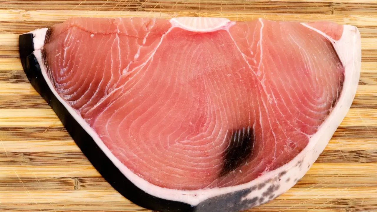 Fetta di tonnina, un pregiato pesce azzurro, su tagliere di legno. La sua carne rosa vivo mostra le tipiche striature.