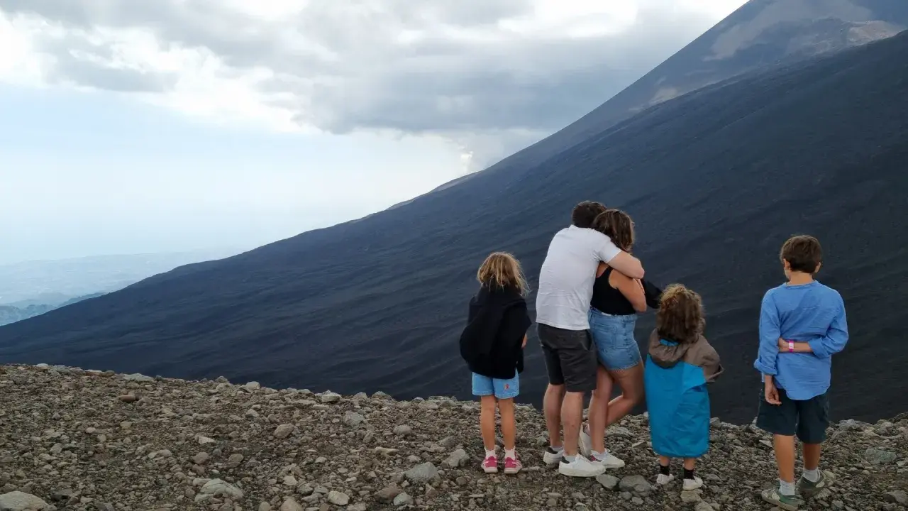 Famiglia in vacanza in Sicilia con bambini, ammira il pendio scuro di un vulcano.