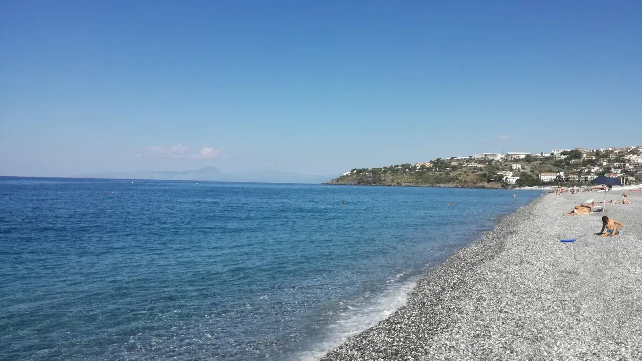 Spiaggia di ciottoli con mare azzurro e case arroccate sulla collina. Una giornata perfetta per godersi la **scalinea mare**.
