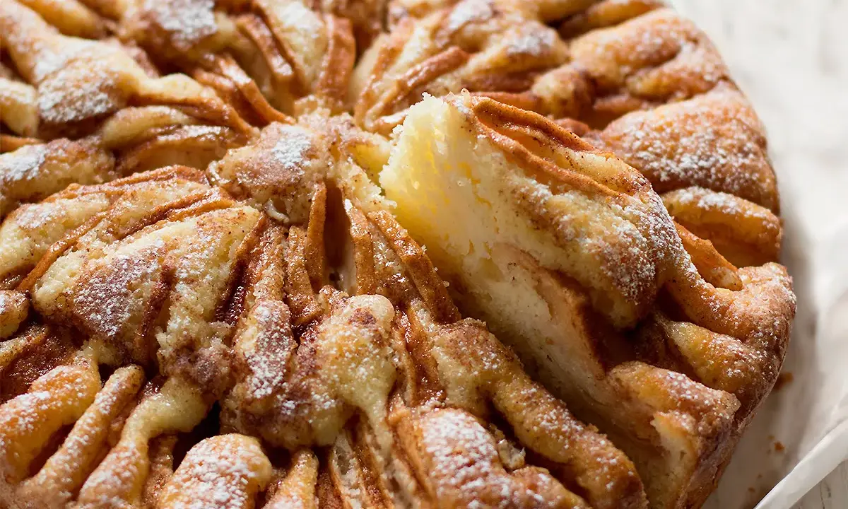 Una deliziosa torta di mele, con fette di mela disposte a raggiera e spolverata di zucchero a velo.
