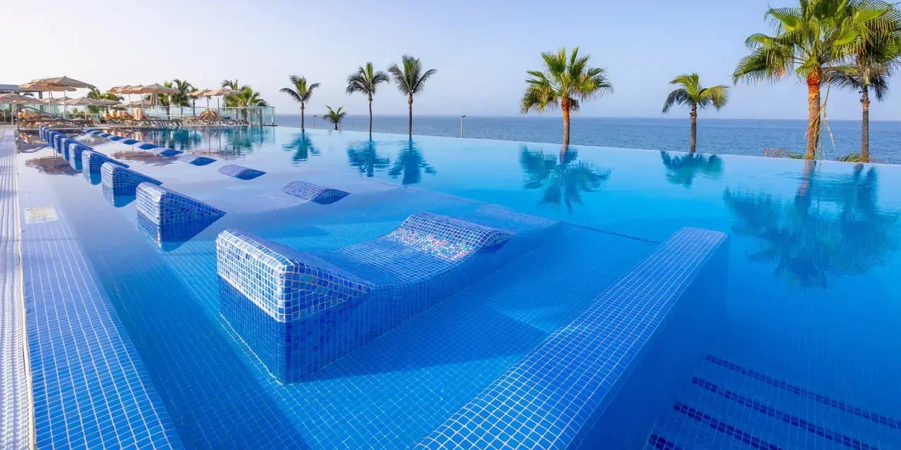 Piscina a sfioro con lettini integrati e palme, vista mare. Un sogno al searesort Riu Gran Canaria.