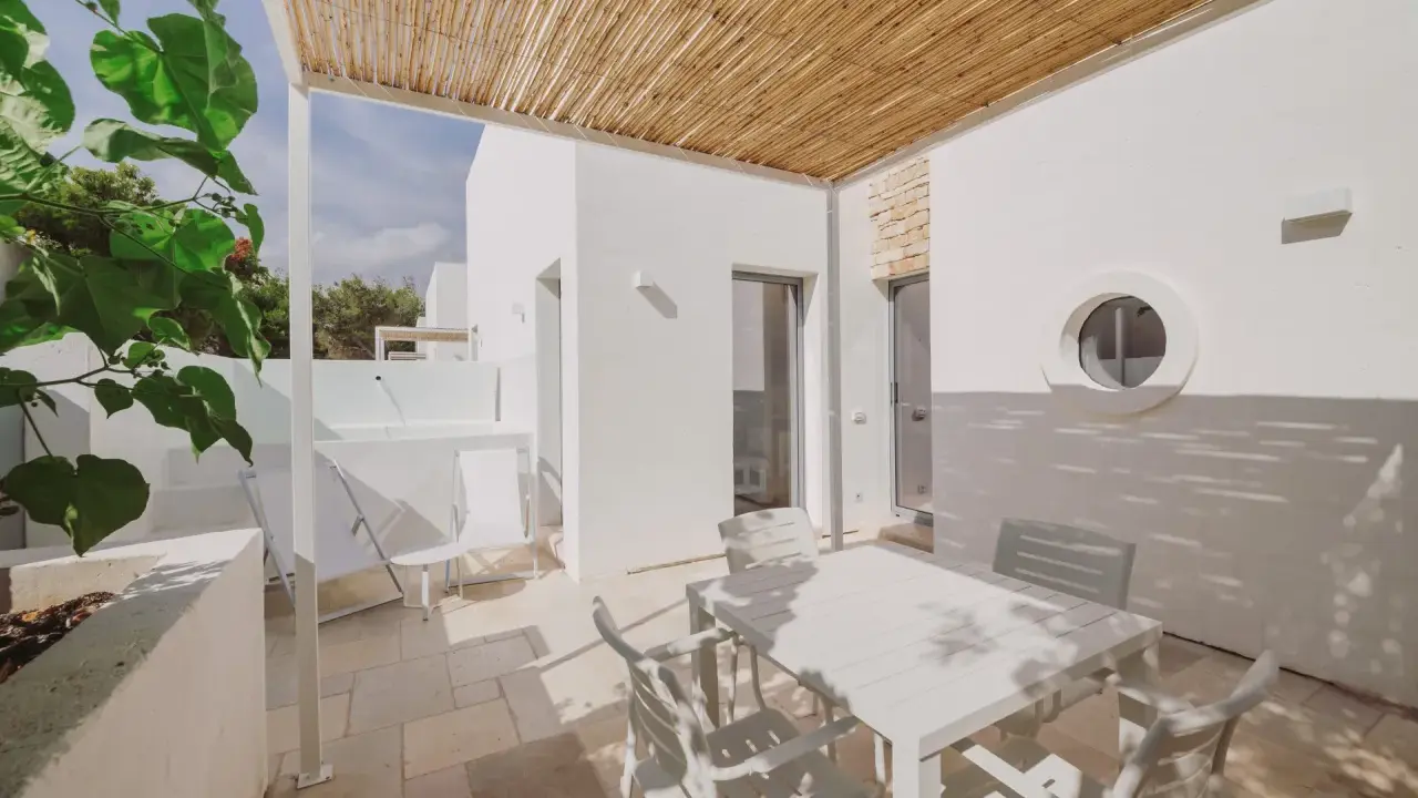 Terrazza con tavolo e sedie bianche, tettoia in bambù, tipica del Nicolaus Club Meditur Village.