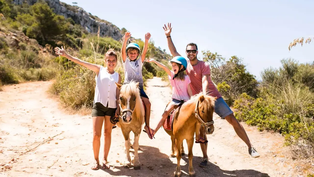 Famiglia felice a Minorca con bambini a cavallo, un'avventura indimenticabile tra sentieri soleggiati e natura rigogliosa.