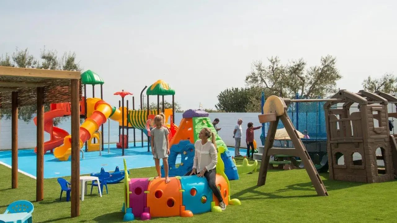 Un parco giochi colorato in una masseria per bambini in Puglia, con scivoli, tunnel e altalene. Famiglie si divertono sotto il sole.