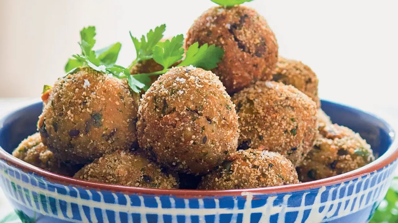 Polpette di melanzane dorate e croccanti, guarnite con prezzemolo fresco, in una ciotola blu decorata.