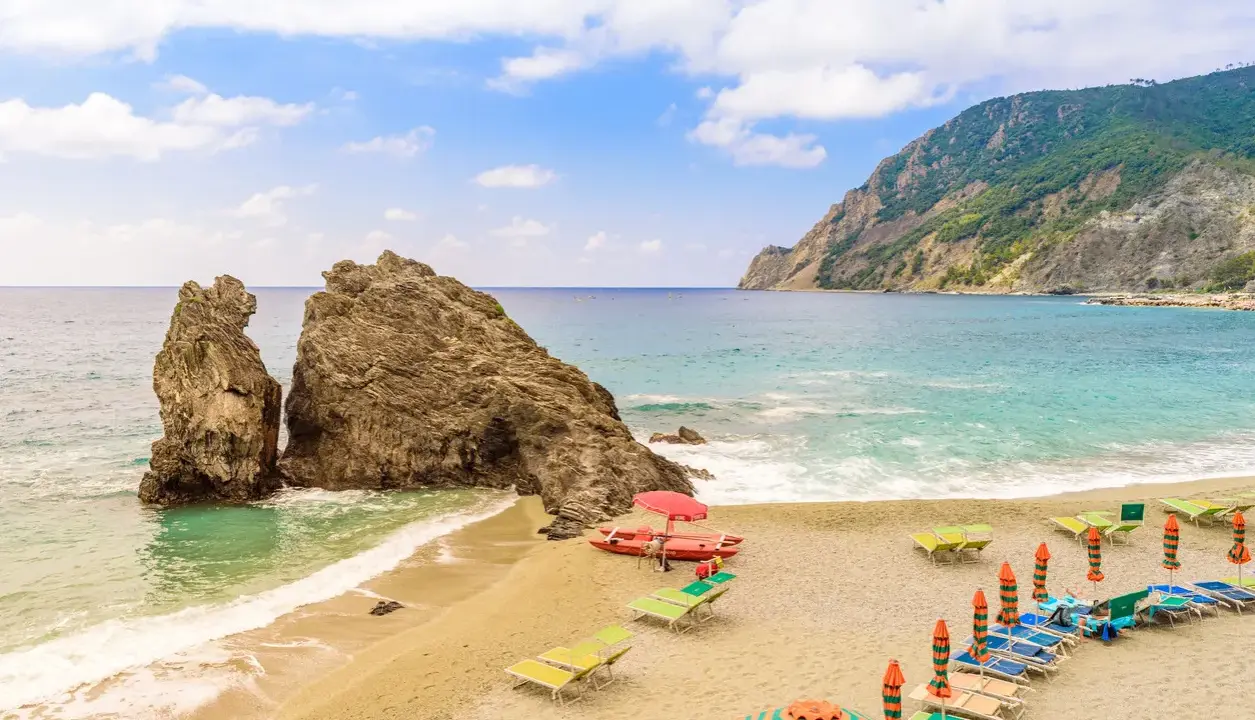 Spiagge sabbia Liguria: scogli imponenti, mare turchese e lettini pronti per il relax.