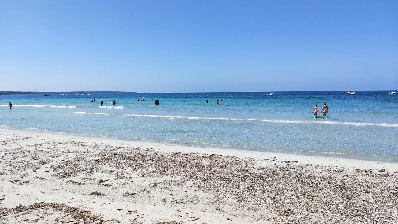 Spiaggia di Arbatax con sabbia chiara e mare cristallino, bagnanti e barche all'orizzonte. Un angolo di paradiso che ricorda la spiaggia rosa.
