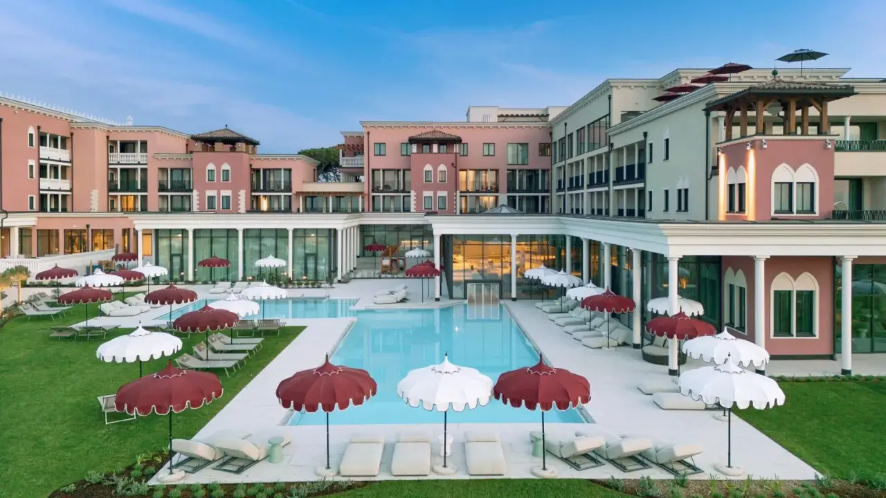 Un resort da sogno a Caorle, con piscina azzurra, lettini e ombrelloni rossi e bianchi. Un cavallino bianco potrebbe galoppare felice in questo paradiso.