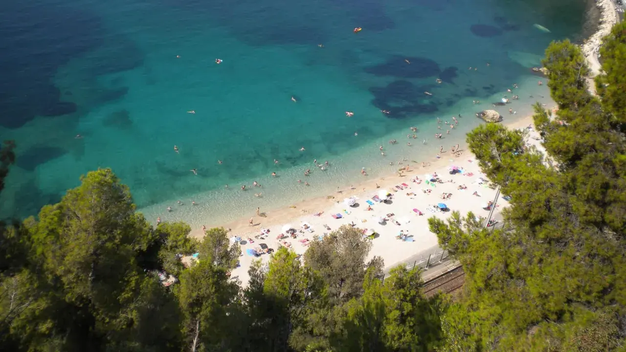 Spiaggia affollata sulla costa azzurra con bambini che giocano in acqua e prendono il sole.