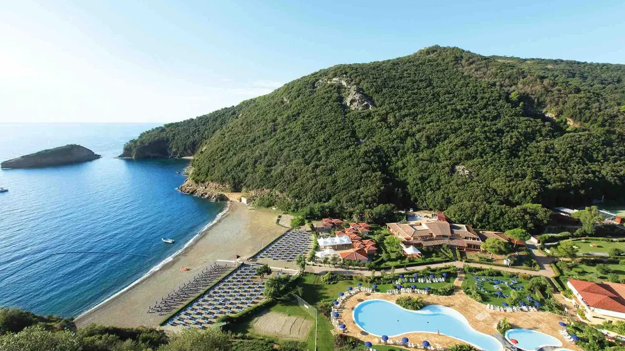 Villaggio toscana sul mare con spiaggia attrezzata, piscine e rigogliosa vegetazione che abbraccia la costa.