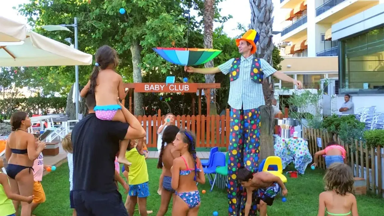 Hotel con biberoneria: animazione al Baby Club con un clown che intrattiene i bambini con palline colorate e un ombrello arcobaleno.