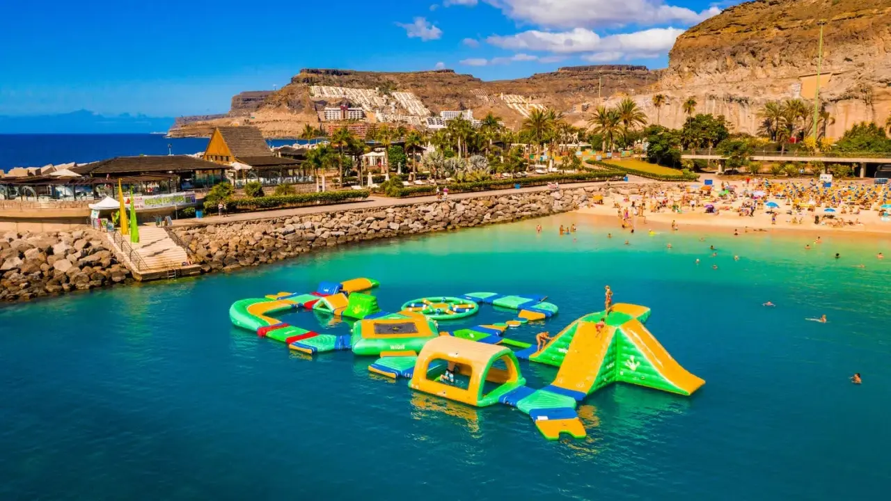 Divertimento acquatico a Gran Canaria con bambini: scivoli gonfiabili e giochi in mare su una spiaggia affollata.