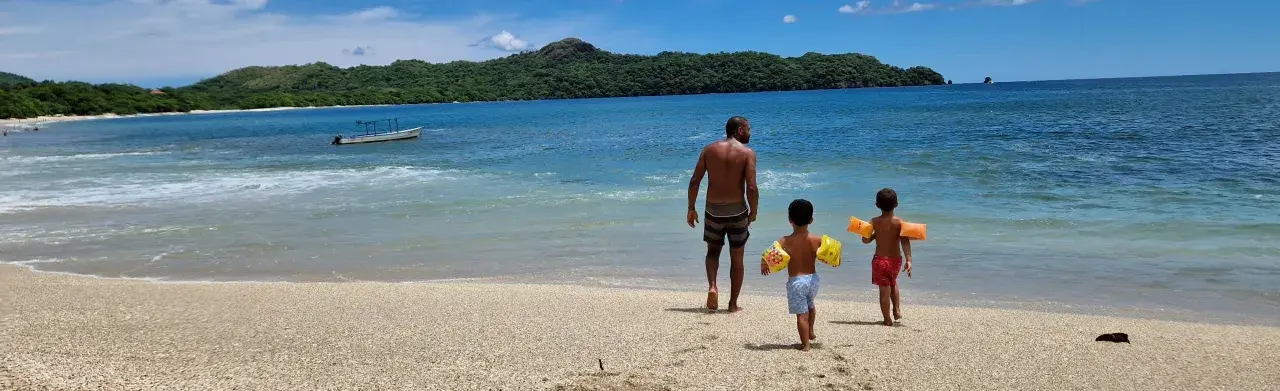 Un padre cammina sulla spiaggia con i suoi due figli, pronti per un'avventura in Costa Rica con bambini.