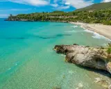 Spiaggia dorata e mare cristallino nel Cilento, con una torre antica su una scogliera e colline verdi sullo sfondo.