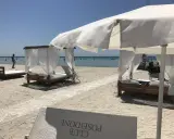 Beach cabanas with white curtains and beds on a sandy beach with the ocean in the background.