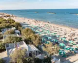 Lidi ferraresi: una distesa di ombrelloni verdi e bianchi sulla sabbia dorata, con il mare azzurro e alcune persone che si godono il sole.