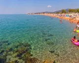Spiaggia affollata a Santa Susanna, Spagna, con persone che nuotano e si rilassano in un mare cristallino.