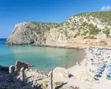 Spiaggia affollata con ombrelloni colorati, acque cristalline e scogliere verdi. Perfetta per vacanze al mare economiche e rilassanti.