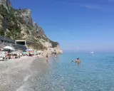 Varigotti spiaggia più bella: gente rilassata sotto gli ombrelloni, mare cristallino e scogliere imponenti.