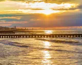 Tramonto dorato sul mare veneto, con moli che si estendono nell'acqua e una città all'orizzonte.