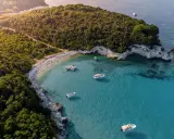 Baia con acque cristalline e vegetazione lussureggiante, ideale per famiglie. Diverse barche ormeggiate, perfette per esplorare le isole greche.