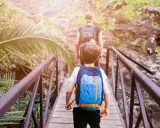 Bambini con zaini attraversano un ponte di legno in un sentiero lussureggiante, un'avventura perfetta per il tuo viaggio a Tenerife con bambini.