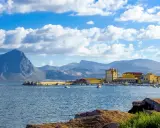 La tonnara di Bonagia, con il suo porto e le montagne sullo sfondo, sotto un cielo azzurro e nuvoloso.