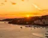 Tramonto dorato sul mare in Slovenia, con un porto pieno di barche e una costa verdeggiante. Immagina i bambini che giocano felici sulla spiaggia.